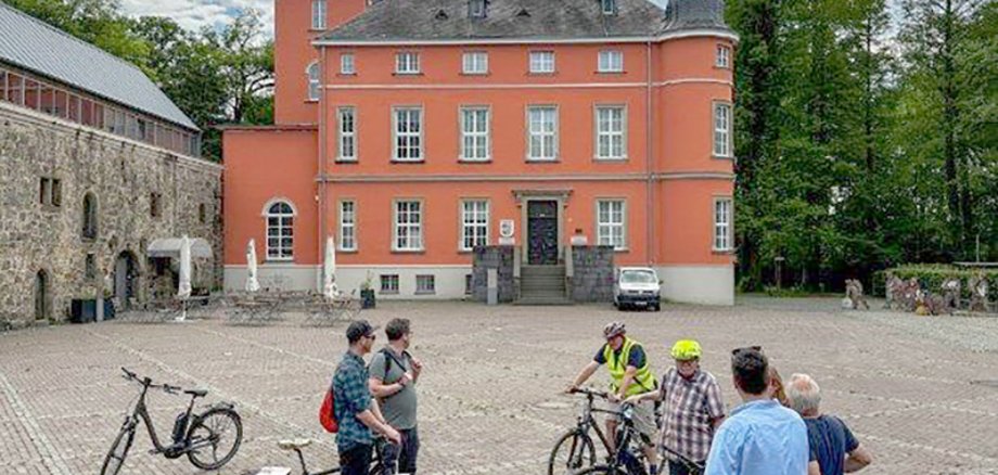 Menschen auf einem Fahrrad vor Burg Wissem